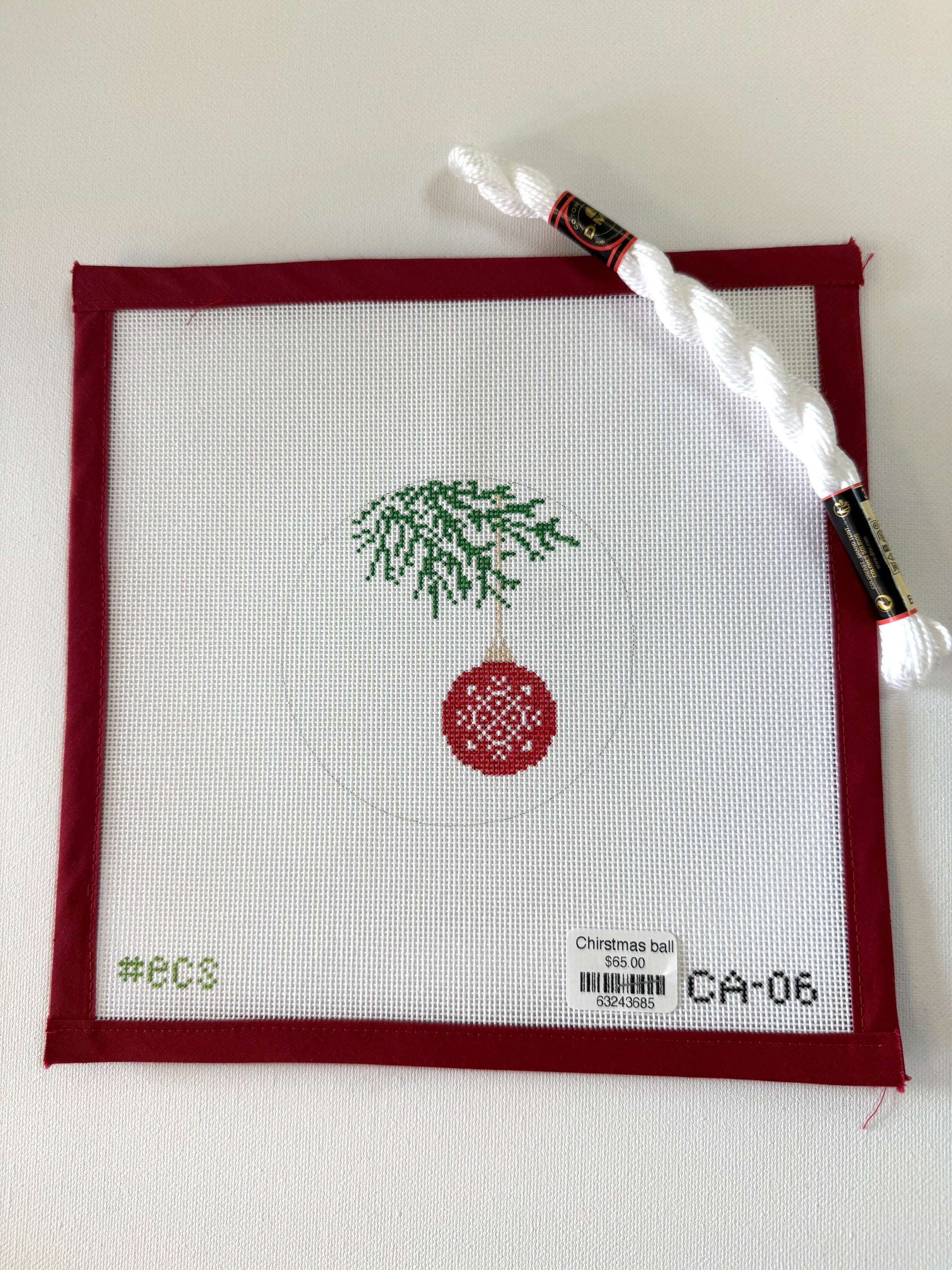 Cross-stitched design of a Christmas ball with a tree on fabric, with a needle and thread in the background.