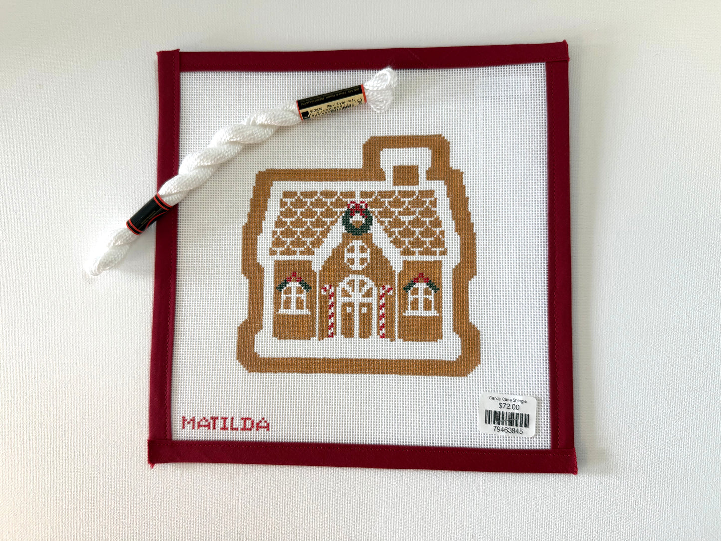Cross-stitched gingerbread house design on fabric with a pen and thread on a white background
