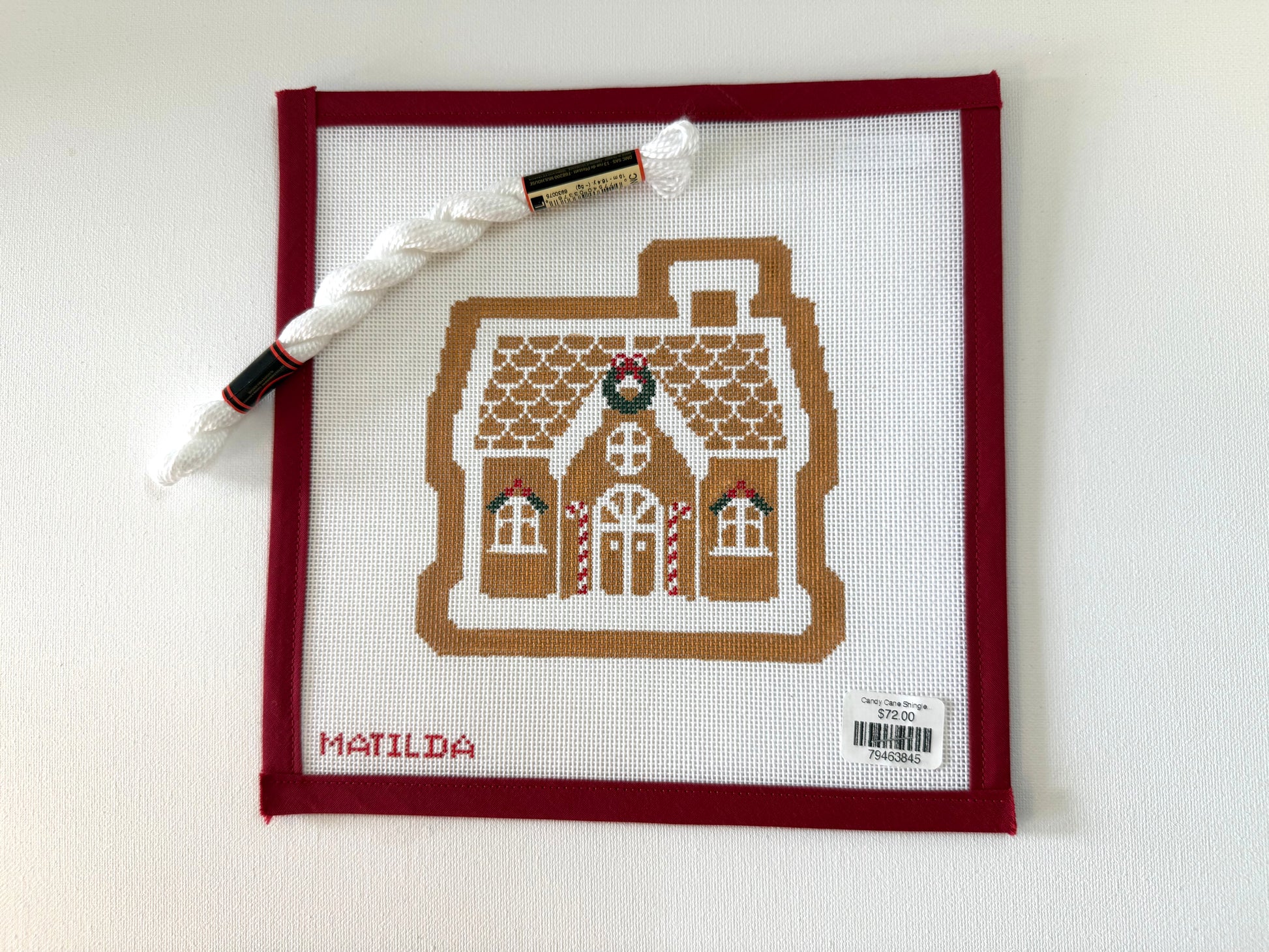 Cross-stitched gingerbread house design on fabric with a pen and thread on a white background