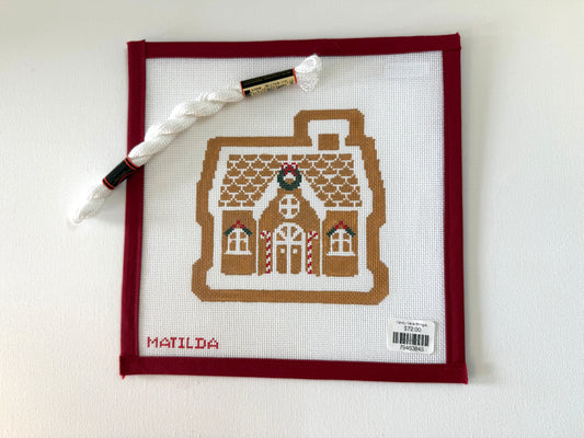 Cross-stitched gingerbread house design on fabric with a pen and thread on a white background