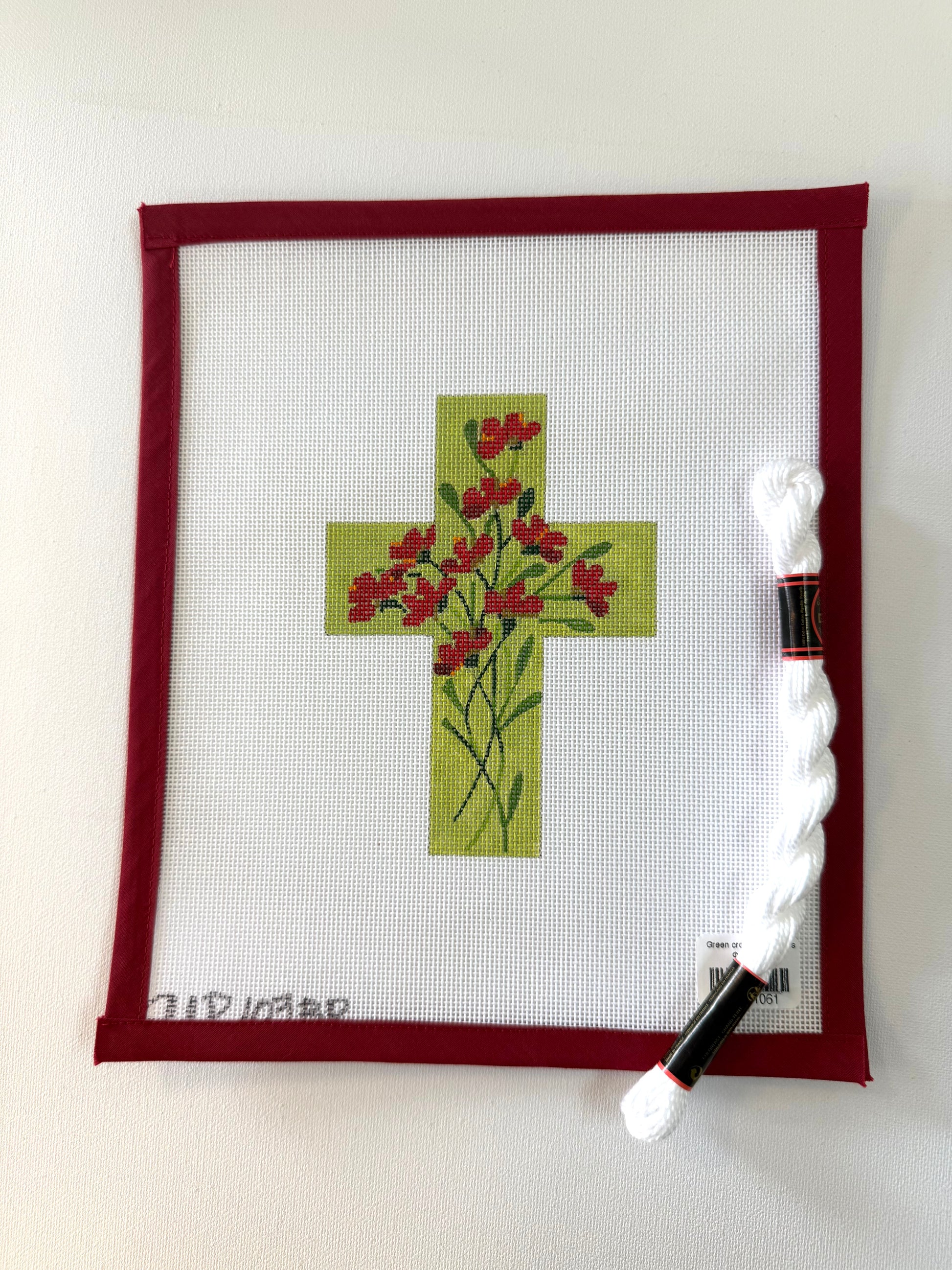 Cross-stitched design with red flowers on white fabric, framed in red, next to a spool of thread.